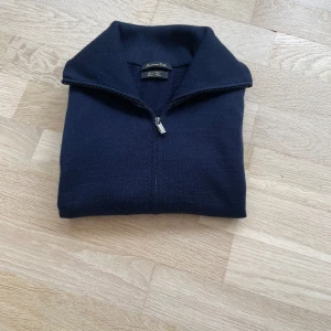 Marinblå kofta från Massimo Dutti - Klassisk marinblå kofta från Massimo Dutti med hel dragkedja och hög krage. Tröjan är stickad i mjukt material och har långa ärmar samt ribbade muddar. Perfekt för lager-på-lager och enkel att matcha med jeans eller chinos. Modellen är 176 cm