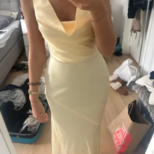 Ljusgul balklänning med öppen rygg - Säljer en elegant ljusgul långklänning i satinliknande material. Köpte här på Plick av en tjej som sa att den var från en butiqe i Frankrike. Klänningen har en snygg draperad urringning, smal passform och öppen rygg med knytband. Perfekt för dig som vill sticka ut med en stilren och modern look. Passar till speciella tillfällen som balen och ger en lyxig känsla.