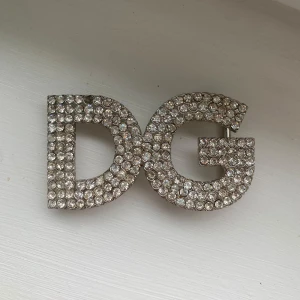 Glittrigt DG bältesspänne i silver - Säljer ett fett DG bältesspänne från Dolce & Gabbana, täckt med glittrande stenar i silverfärg