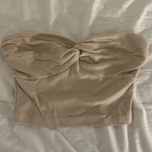 Beige ribbad bandeau tubtopp från SHEIN - Säljer en beige bandeau tubtopp från SHEIN i storlek XS. Toppen är ribbad och har en snygg twistad detalj framtill.