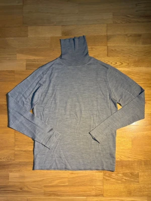 Grå polotröja från Filippa K - Säljer en stilren grå polotröja från Filippa K i storlek M. Tröjan har lång ärm och hög polokrage, perfekt för lager-på-lager. Materialet är mjukt och tunt, vilket gör den skön att bära både till jeans och dressade byxor.