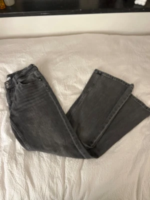 Grå bootcut jeans från Cubus - Snygga grå jeans från Cubus med bootcut passform. Jeansen har en mörkgrå tvätt och är gjorda i slitstarkt denim. Bakfickorna har lock och silverfärgade knappar. 