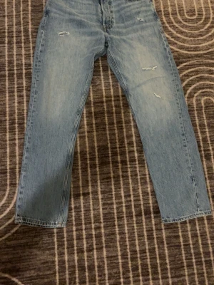 Ljusblå jeans från Jack & Jones - Säljer ett par ljusblå jeans från Jack & Jones med klassisk femficksdesign och slitna detaljer framtill. Jeansen har rak passform och är tillverkade i jeansmaterial med snygga kontrastsömmar. Perfekt för dig som gillar en chill och avslappnad stil. 