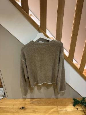 stickad tröja från Kappahl - Mysig beige stickad tröja från Kappahl i storlek 158/164. Tröjan har lång ärm och vita detaljer längs kanterna. Perfekt för dig som gillar enkel och stilren design med en chill vibe.