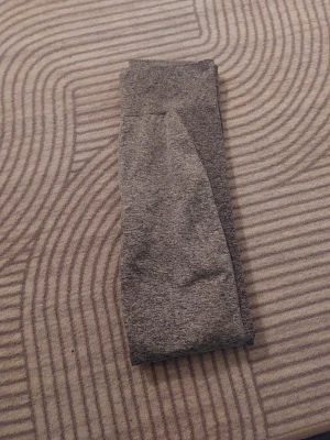 Grå Gymshark leggings - Säljer ett par grå leggings från Gymshark med hög midja och bred resår med logga. Materialet är mjukt och stretchigt, perfekt för träning eller chill. Snyggt melerat tyg och tight passform som sitter skönt hela dagen.