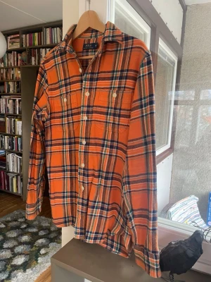 Flanell skjorta från Polo Ralph Lauren - Säljer en snygg orange rutig skjorta från Polo Ralph Lauren i storlek S. Skjortan har klassisk krage, två bröstfickor med knappar och långa ärmar. Materialet är mjuk bomull och färgerna är orange, blå, grön och vit. Perfekt för dig som gillar färg och mönster.