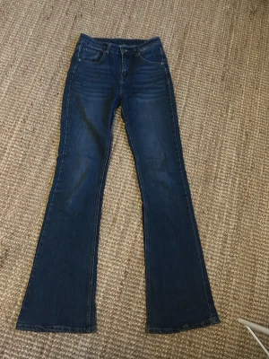 Bootcut jeans i mörkblå denim, S - Snygga bootcut jeans i mörkblå denim med klassisk femficksdesign. Byxorna är tillverkade av bomull, viskos och elastan för en skön och flexibel passform. Perfekta för dig som gillar en lite vidare siluett nertill och vill ha en tidlös look.