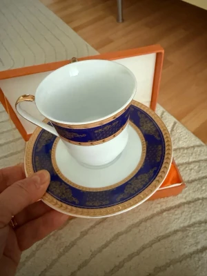 Ny kaffeservis i porslin – vit/blå med guldkant -  Säljer en kaffeservis i porslin bestående av vita koppar med tillhörande fat, dekorerade med blått mönster och guldkant. Klassisk och tidlös design som passar både till vardag och fest.  Servisen är helt ny och ligger kvar i originalkartong.