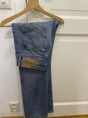 Vintage Denim and Supply Ralph Lauren blå jeans  - Säljer ett par blå jeans från Denim & Supply Ralph Lauren med raka ben och snygga slitningar på både fram- och baksida. Jeansen har klassisk femficksdesign, normal passform och är gjorda i tåligt jeanstyg. Dessvärre är jeanskanppen av, därav det billiga priset. Går att åtgärda genom att sy en knapp 