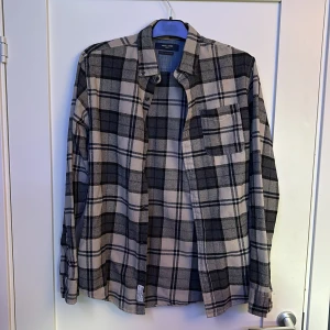 Rutig skjorta från Jack & Jones  - Snygg rutig skjorta från Jack & Jones i svart och beige. Skjortan har klassisk krage, bröstficka och knäppning framtill. Tillverkad i mjukare bomull, perfekt för lager-på-lager-stil. Långärmad och passar dig som gillar en avslappnad look.