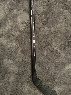 Svart Bauer Tracer mini stick hockeyklubba - Säljer en svart Bauer Tracer hockeyklubba mini stick med stilrena vita och guldiga detaljer längs skaftet. Klubban har en klassisk form med böjd blad och är tillverkad i lätt syntetmaterial för snabb hantering på isen. Perfekt för dig som vill ha en snygg och modern klubba. Säljer den då jag fick dubbelt. Den tillhör Bauer mystery mini stick kollektionen från iår. Är även öppen för byten. Helt oanvänd. 