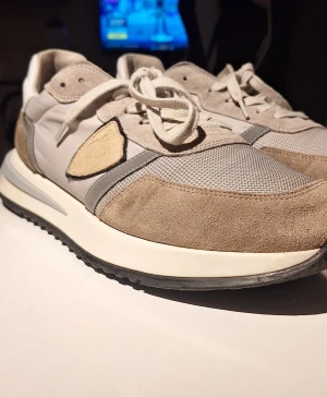 Philippe Model beige sneakers - Snygga sneakers från Philippe Model i beige och grå toner med vit sula. Ovandelen är en mix av mocka, mesh och skinn, med coola detaljer och snörning. Yttersulan är svart och har tydligt mönster för bra grepp. Perfekt för dig som gillar stilrena och trendiga sneakers. Skriv vid frågor eller funderingar!