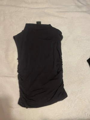 Svart polotopp i mjukt material - Säljer en svart polotopp med ärmlös design och hög krage. Toppen är gjord i ett mjukt och stretchigt material som sitter snyggt mot kroppen. Perfekt att styla med jeans eller kjol för en cool look.