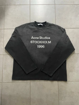 Svart långärmad tröja Acne Studios - Svart långärmad tröja från Acne Studios med tryck 'STOCKHOLM 1996' på bröstet. Tröjan har en klassisk rund hals och är gjord i mjuk bomull. Passformen är loose och den har en enkel, stilren design som funkar till många olika looks.