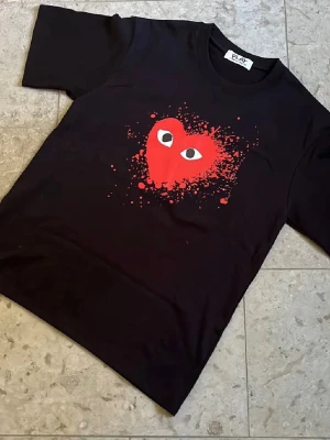 Svart Cdg play tshirt - Svart t-shirt från Cdg Play med ett stort rött hjärta med ögon och färgstänk på bröstet. Nytt skick och fraktas inom 24h✅