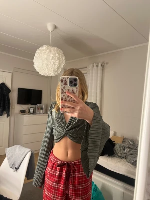 Grå plisserad croppad topp Shein - Säljer en grå plisserad croppad topp från Shein i storlek XS. Toppen har långa utsvängda ärmar och en snygg twist-detalj framtill. Materialet är glansigt och lätt, vilket ger en cool och trendig look.