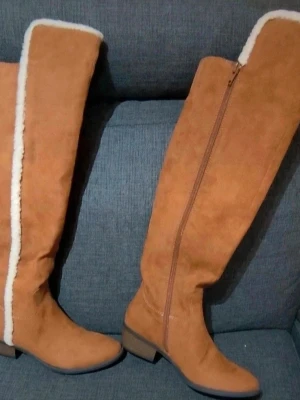 Bruna höga boots  - Säljer ett par snygga höga boots från MIA i brun mocka med vit fuskpäls längs kanten. Skorna har rund tå, låg klack och dragkedja på sidan för enkel påtagning. Perfekta för kalla dagar och ger en cool look till din outfit. Storlek 36