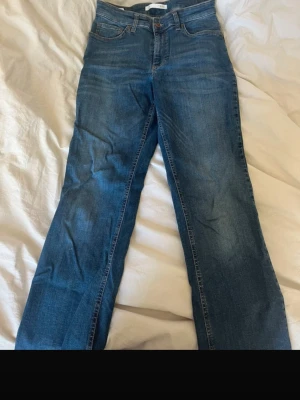 Blå bootcut jeans från MAC, strl 40/30 - Snygga blå jeans från MAC i modellen Melanie, med klassisk femficksdesign och bootcut-snitt. Jeansen är tillverkade av 92% bomull, 5% polyester och 3% elastan för en bekväm passform. Perfekt för dig som gillar en tidlös look med lite utsvängda ben.