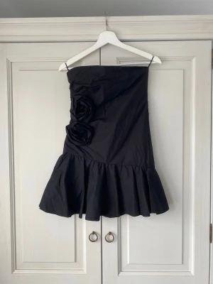 Svart axelbandslös kortklänning med volang - Så fin axelbandslös svart kort klänning med snygga detaljer!! Endast använd någon gång. Perfekt till nyår, jag skickat snabbt! Pris kan diskuteras vid snabb affär 