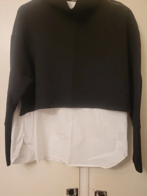 Svart och vit croppad tröja Zara M - Snygg croppad tröja från Zara Trafaluc Collection i svart och vitt. Tröjan har lång ärm och en cool lager-på-lager look med vit skjortdel nedtill. Perfekt för dig som gillar trendiga och unika plagg med lite edge.