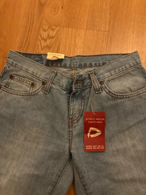 Dallas Jeans 527 ljusblå bootcut/baggy - Säljer ett par Dallas Jeans modell 527 i ljusblå tvätt med klassisk bootcut. Jeansen har fem fickor, orangea sömmar och är tillverkade i jeansmaterial. Passar dig som gillar amerikansk denimstil och vill ha en snygg siluett med lite utsvängda ben.