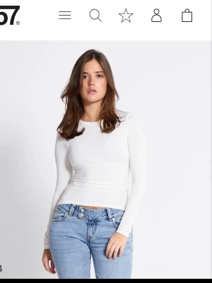 Vit långärmad topp från 157 - En stilren vit långärmad topp från 157 med rund halsringning. Toppen är figurnära och tillverkad i ett mjukt och stretchigt material som passar perfekt till jeans eller kjol. Enkel och clean design som är lätt att matcha med andra plagg.