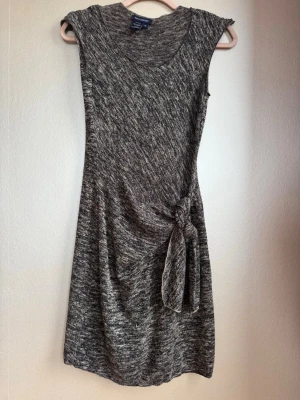 Finstickad klänning Max Edition - Superskön svartmelerad klänning från Max Edition med rund halsringning och coolt knyt nedanför midjan som trollar bort lilla magen. Klänningen är ärmlös och har en mjuk, stretchig känsla tack vare materialblandningen av polyester och rayon. Perfekt för dig som gillar enkel men snygg sti