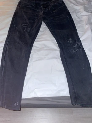 Svarta jeans från Dondup med slitningar - Svarta jeans från Dondup med coola slitningar och distressed detaljer på benen. Klassisk femficksmodell med rak passform och låg midja. Jeansen är gjorda i ett mjukt bomullsmaterial och har en snygg, mörk tvätt som ger en edgy vibe.