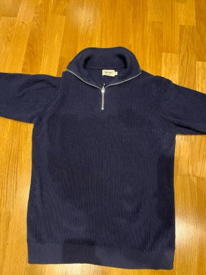 Marinblå stickad tröja med half zip - Säljer en marinblå stickad tröja från East West i storlek M. Tröjan har en hög krage och en snygg half zip-dragkedja framtill. Ribbad struktur och långärmad modell som passar perfekt när det är lite kyligt ute. 