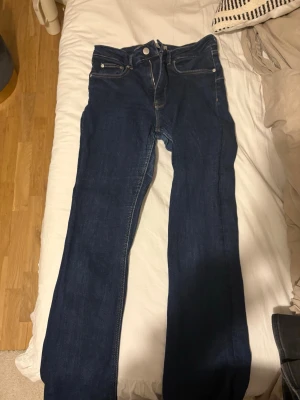 Mörkblå jeans från Zara - Säljer ett par mörkblå Zara jeans med klassisk femficksdesign och bootcut. Jeansen har silverfärgade knappar och dragkedja framtill. Materialet är slitstarkt denim i bomull och passformen är normal med lite smalare ben.