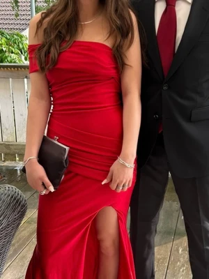 Röd axelbandslös balklänning med slits - Säljer en snygg röd balklänning med axelbandslös design och figurnära passform. Klänningen har en hög slits framtill och draperade detaljer som ger en elegant look. Perfekt för bal eller fest. Materialet känns mjukt och följsamt. Använd en gång!!! 