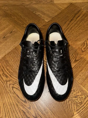 Nike Hypervenom Phantom fotbollsskor svart/gul, stl 41 - Säljer ett par Nike Hypervenom Phantom fotbollsskor med svart ovandel, vit swoosh och coolt mönster i blått och gult på sidorna. Storlek 41. Använda endast ett fåtal gånger. Väldigt ovanliga och eftertraktade. Originalsulor medföljer inte, men ett par andra. Skopåse medföljer. Priset är aningen förhandlingsbart. 
