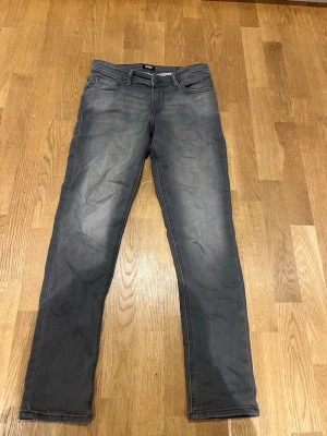 Grå slim jeans från Jack & Jones - Snygga grå jeans från Jack & Jones i modellen Glenn slim. Jeansen har fem fickor, bälteshällor och klassisk knapp- och dragkedjestängning. Materialet är mjukt och stretchigt jeans, perfekt för dig som gillar en smalare passform.