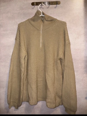 Beige stickad tröja med half zip - Säljer en beige stickad tröja med hög krage och half zip. Tröjan har en loose passform och är långärmad med ribbade muddar. Perfekt för kyliga dagar och enkel att matcha med jeans eller mjukisbyxor.