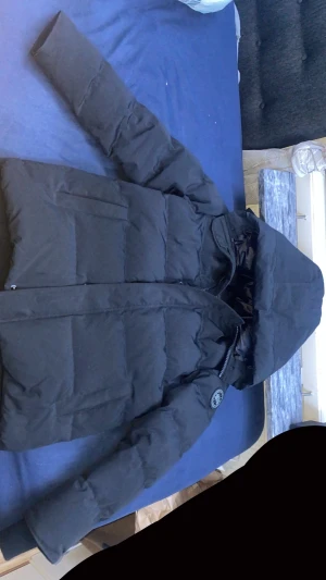 Svart pufferjacka från Canada Goose - Säljer en sprillans ny svart pufferjacka Canada Goose med huva och snyggt broderat märke på ärmen. Har använt jackan bara 2 ggr och säljer den för jag fick en annan jacka som present, pris kan diskuteras 