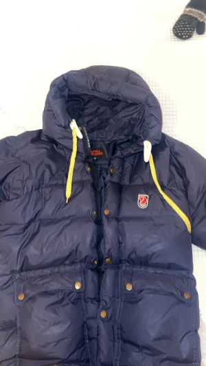 Mörkblå dunjacka från Fjällräven XS - Snygg mörkblå dunjacka från Fjällräven med gul snörning. Inga hål eller fläckar💖 Storlek xs