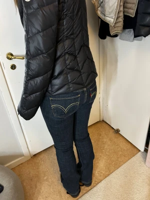 Levi's 527 mörkblå bootcut jeans - Mörkblå Levi's 527 jeans med klassiska kontrastsömmar och femficksmodell. Snygg bootcut-passform som sitter tajt över låren och släpper ut vid anklarna. Tillverkade i slitstarkt denim med låg midja och ikoniska Levi's-detaljer på bakfickorna.