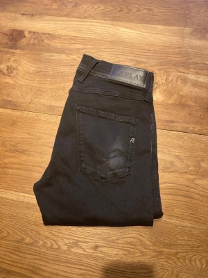 Svarta Replay Anbass, W30, L32 - Svarta Replay Anbass jeans med klassisk design. Jeansen har rak passform och normal midja, med Replay-logga på bakfickan och läderpatch i midjan. De är i storlek W30, L32.