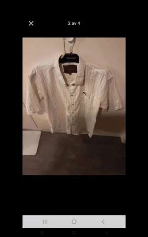 Vit randig skjorta med kort ärm - Fräsch vit skjorta från KappAhl med tunna ränder i olika färger. Skjortan har korta ärmar, klassisk krage och knappar framtill. Perfekt för dig som gillar en clean och chill stil med lite färg. Finns en liten broderad detalj på bröstet.