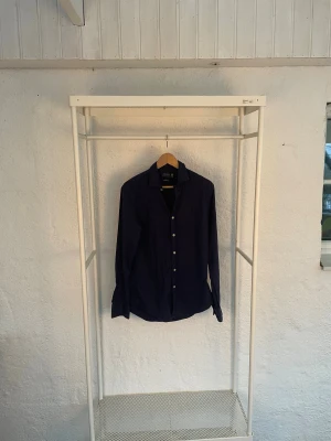 Mörkblå skjorta Polo Ralph Lauren M - Snygg mörkblå skjorta från Polo Ralph Lauren i slim fit. Tillverkad i lätt bomullstwill, med klassisk krage, långa ärmar och knäppning framtill. Perfekt för dig som gillar stilrena och tidlösa plagg.