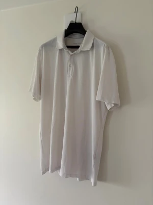 Vit golfpiké från Galvin Green - Vit golfpiké från Galvin Green med klassisk krage och knappar framtill. Tröjan har korta ärmar och diskret logga på ärmen samt i nacken. Perfekt för golf eller andra sportiga aktiviteter. Storlek: L passar M. Nypris: 999kr