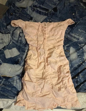 Ljusrosa offshoulder kortklänning - Supersöt ljusrosa kortklänning med offshoulder och snörning framtill. Klänningen har rynkade detaljer över hela och volangkant nertill. Perfekt för dig som gillar romantisk och feminin stil. Materialet känns lätt och somrigt.