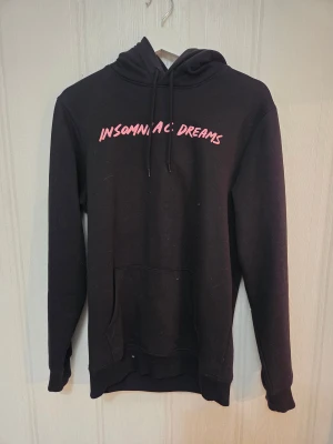 Svart hoodie från HM - Svart hoodie från HM med rosa text 'INSOMNIAC DREAMS' på bröstet och en stor grafisk print på ryggen. Tröjan har huva med snörning och en klassisk magficka.