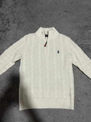 Vit stickad tröja Polo Ralph Lauren - Snygg vit kabelstickad tröja från Polo Ralph Lauren med halv dragkedja och ribbad krage. Den är som ny, har använd den bara några gånger. Priset kan diskuteras!