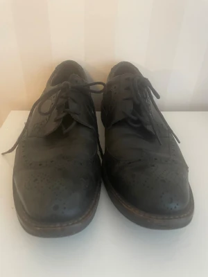 Svarta brogues i skinn med snörning - Klassiska Ecco svarta brogues med snygga perforerade detaljer och snörning. Skorna har rund tå och är tillverkade i skinn med en låg klack. Perfekta för dig som gillar en dressad och tidlös stil.