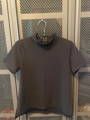 Svart polotopp från Boohoo - Säljer en svart polotopp från Boohoo i storlek 34. Toppen har korta ärmar, hög krage och en dold dragkedja bak i nacken. Materialet är slätt och stretchigt, vilket ger en clean och stilren look. Perfekt att styla med jeans eller kjol för en trendig vibe.