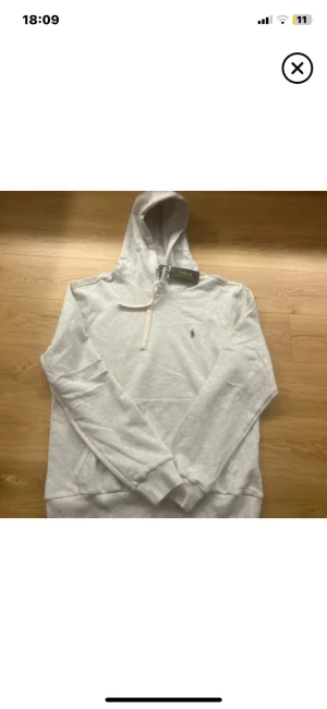 Vit hoodie från Polo Ralph Lauren - Snygg vit hoodie från Polo Ralph Lauren med klassisk logga på bröstet. Tröjan har huva med snörning, ribbade muddar och en skön passform. Perfekt för chill dagar och enkel att matcha med jeans eller joggers.