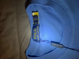 Blå t-shirt från Polo Ralph Lauren - Snygg blå t-shirt från Polo Ralph Lauren i storlek M. Klassisk design med korta ärmar och rund hals. T-shirten har den ikoniska broderade loggan på bröstet och är gjord i mjuk bomull som känns skön mot huden. Perfekt för dig som gillar stilrena och tidlösa plagg.