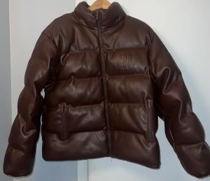 Brun pufferjacka från Wasted Paris - Säljer en brun pufferjacka från Wasted Paris i syntetmaterial med skinnlook. Jackan har avtagbar huva, dragkedja framtill och två fickor med dragkedja. Broderad logga på bröstet och stor Wasted Paris-text på ryggen. Perfekt för kalla dagar. Sorry för dåliga bilder men säg bara till om du vill ha en böttre bild även video.