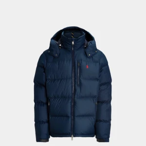 Mörkblå dunjacka Polo Ralph Lauren - Snygg mörkblå dunjacka från Polo Ralph Lauren med huva och dragkedja. Jackan har en klassisk puffer-design, flera fickor med dragkedja och den ikoniska röda Polo-loggan på bröstet. Jackan har små revor och spännet är lite sliten, annars perfekt för kalla dagar och har en clean, modern look.